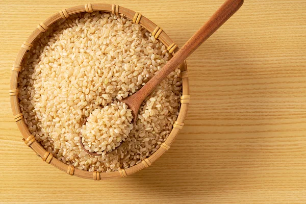 用竹子做的糙米和木制背景的木制勺子 一堆糙米 直接从上往下看的组成 — 图库照片