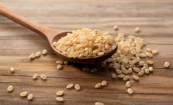 Tahta bir arka planda tahtadan bir kaşıkta kahverengi pirinç. Esmer pirinç yığını.. 