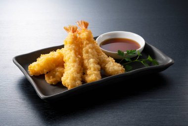 Siyah arka planda duran bir tabakta karides tempurası. Tempura bir Japon yemeğidir. Japon kızarmış karidesi..