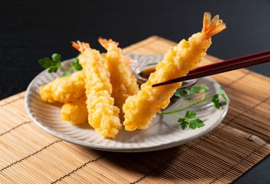 Siyah arka planda duran bir tabakta karides tempurası. Tempura bir Japon yemeğidir. Japon kızarmış karidesi..