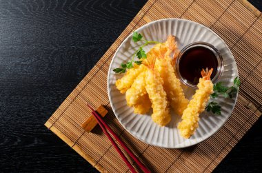 Siyah arka planda duran bir tabakta karides tempurası. Tempura bir Japon yemeğidir. Japon kızarmış karidesi. Yukarıdan görüntüle