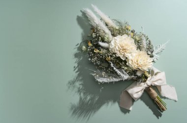 Yeşil arka plana yerleştirilmiş bir buket kurumuş çiçek. Düğün ve kutlama konsepti.