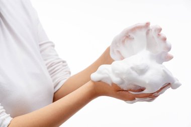 Beyaz arka planda sabun köpüğü tutan kadın. Beyaz baloncuklu eller. Kadın elinin üzerinde beyaz sabun köpüğü dokusu.