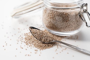 Beyaz arka plana yerleştirilmiş kaşık ve beyaz chia çekirdekli cam kap. Yakın çekim..