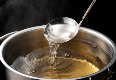 Dashi, soup stock, and the basics of Japanese cuisine. Black background. Steam. Scooping with a ladle.