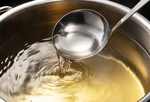Dashi, soup stock, and the basics of Japanese cuisine. Black background. Steam. Scooping with a ladle.
