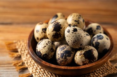 Quail eggs in a wooden bowl placed against a wooden background. 