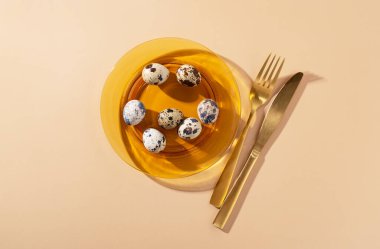 Quail eggs in a glass dish placed on a beige background. An image of the dish. View from above.