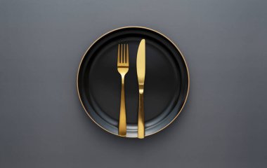 Gold knives and forks on a black background, empty black plate. Beautiful gold cutlery. View from above.