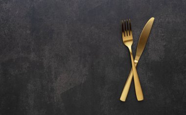 Gold knives and forks set against a black background. Beautiful gold cutlery. View from above.