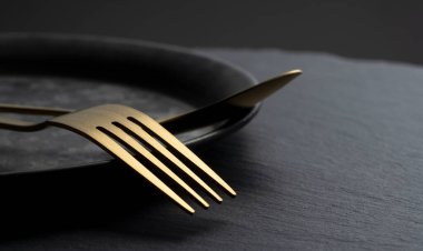 Gold fork and spoon placed on a black iron plate. Beautiful gold cutlery.