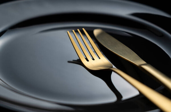 A golden knife and fork on a black plate. Beautiful gold cutlery. Close-up.