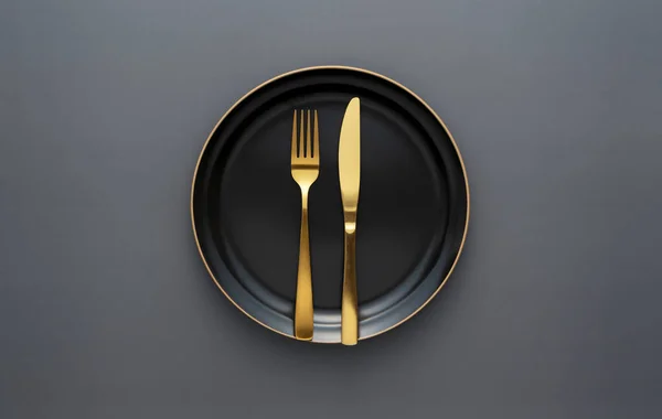 Gold knives and forks on a black background, empty black plate. Beautiful gold cutlery. View from above.