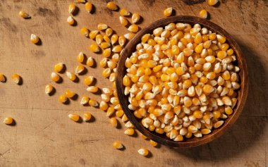 Ahşap bir arka plana yerleştirilmiş tahtadan bir kasede kurumuş mısır taneleri. Patlamış mısır için mısır. Yukarıdan görüntüle.