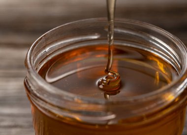 Cam bir kapta eski ahşap bir arka planda duran bal. Damlayan bal. Yakın plan..