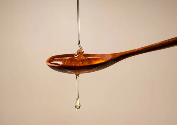 蜂蜜和米色背景的木制勺子 蜂蜜从勺子上滴下 后续行动 — 图库照片