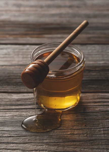 古い木製の背景にガラス容器に蜂蜜と木製の蜂蜜のディッパー 蜂蜜のディップから滴下 — ストック写真