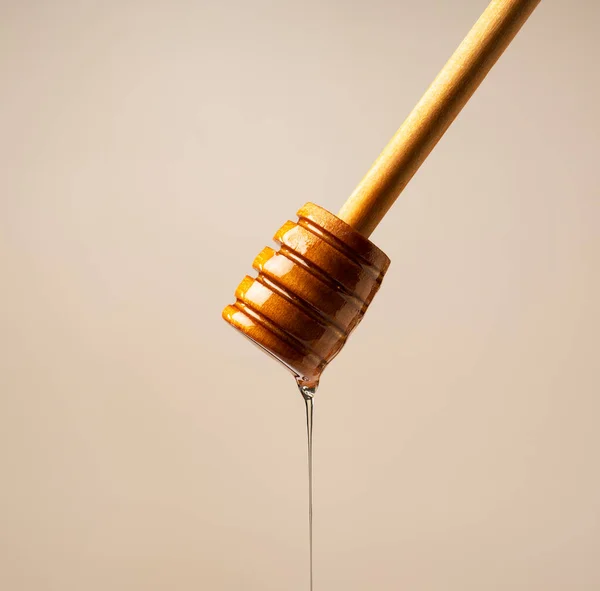 蜂蜜和木制蜂蜜调酒师米色背景 蜜糖从蜜糖搅拌器滴下 后续行动 — 图库照片