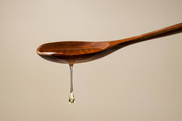Honey and wooden spoon on beige background. Honey dripping from spoon. Close-up.