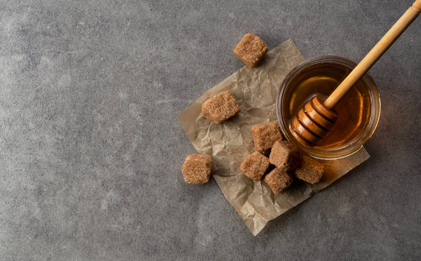 Brown sugar with honey and wooden honey dipper on stone background. Image of beauty. View from above.