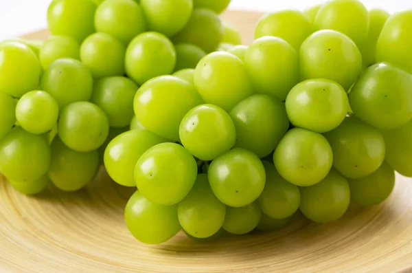 Shine Muscat in a wooden dish on a white background. White grapes. Japanese grapes.