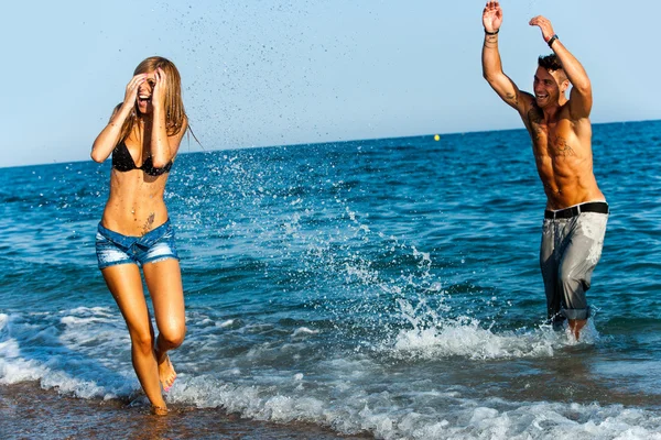 Jeune couple attrayant éclaboussant l'eau au bord de la mer . — Photo