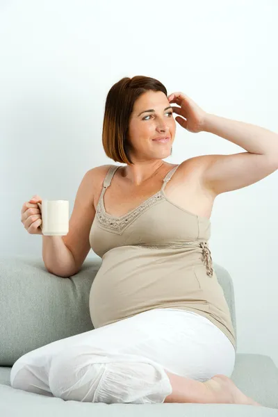 Mulher grávida bebendo café no sofá . — Fotografia de Stock