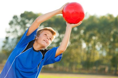 Young boy catching red ball outdoors. clipart