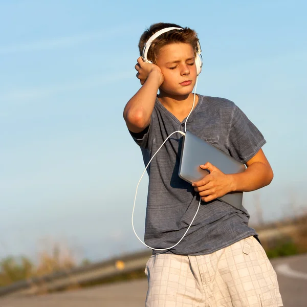 Мальчик наслаждается музыкой на планшете на улице . — стоковое фото
