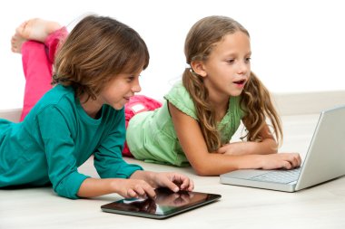 dizüstü ve tablet ile katta iki çocuk.