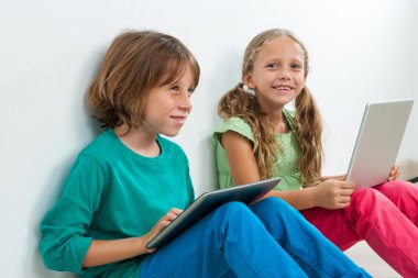 dizüstü bilgisayar ve dijital tablet ile oturan iki çocuk.