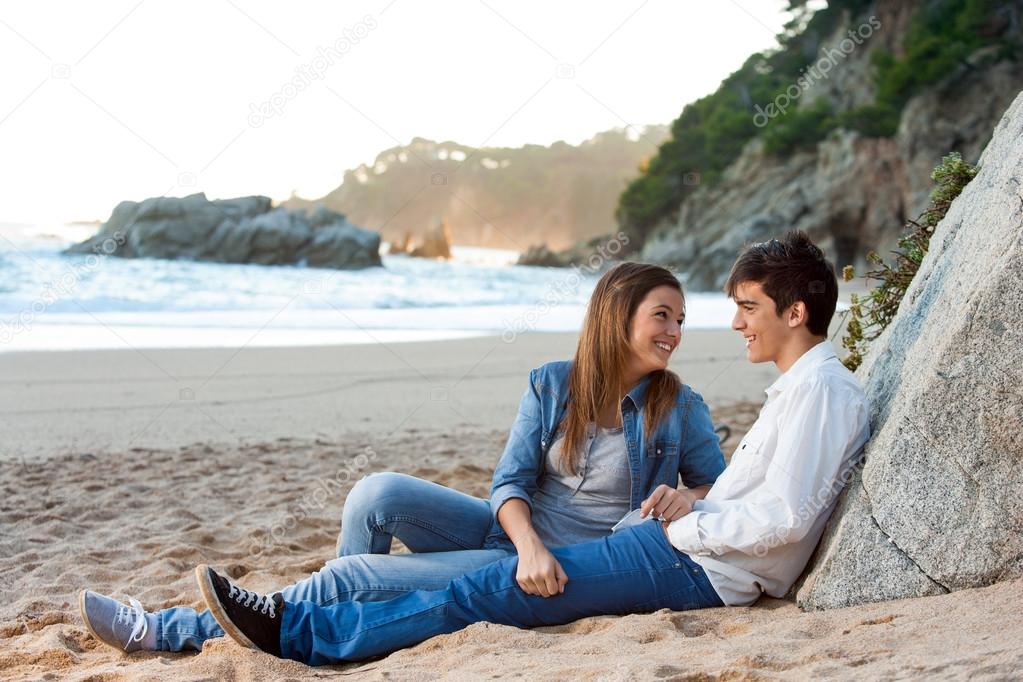 Young handsome couple sitting on beach.