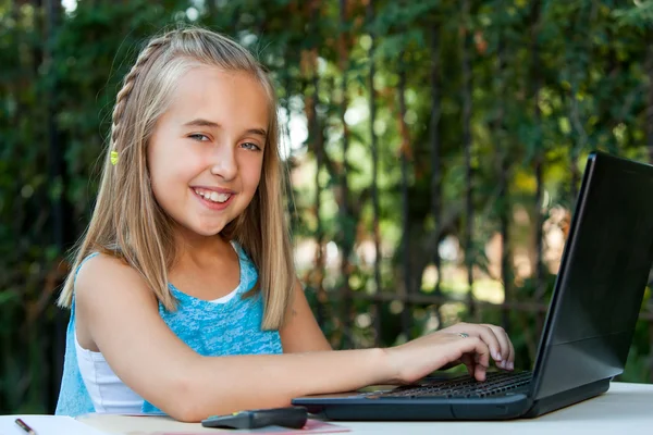 Fille mignonne faisant des devoirs sur ordinateur portable à l'extérieur . — Photo