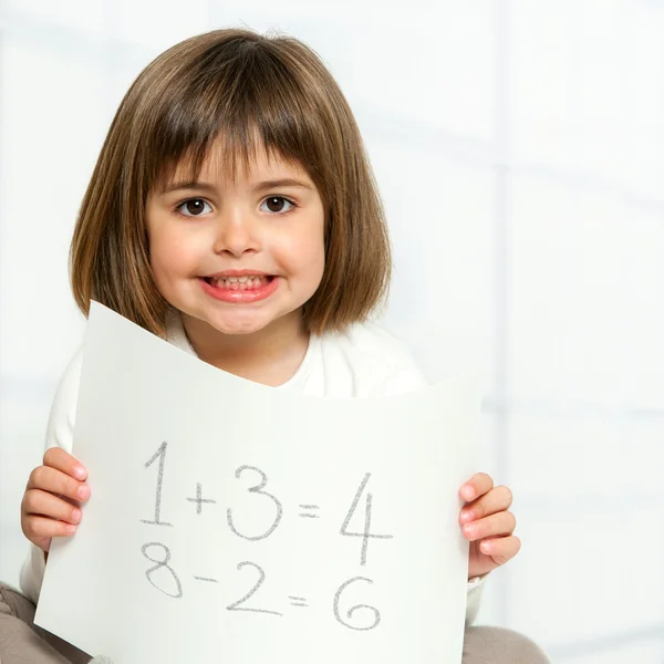 Aranyos lány mutatja a matematikai összegeket a papír. — Stock Fotó