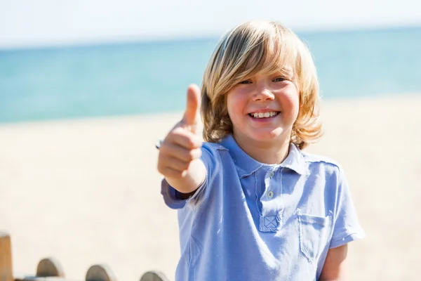 Schattige blonde jongen doen duimen omhoog op strand. — Stockfoto