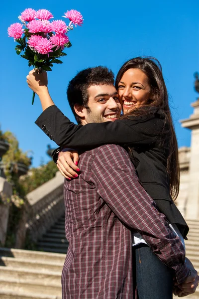 Girl embracing boyfriend with flowers in hand. Stock Photo