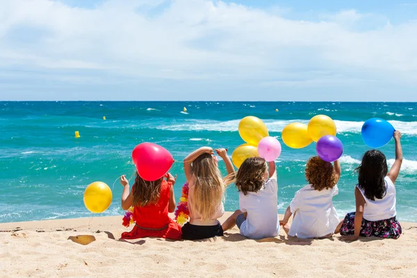 Crianças sentadas na praia com balões coloridos . — Fotografia de Stock