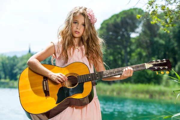 Симпатичная девушка играет на гитаре у озера . — стоковое фото