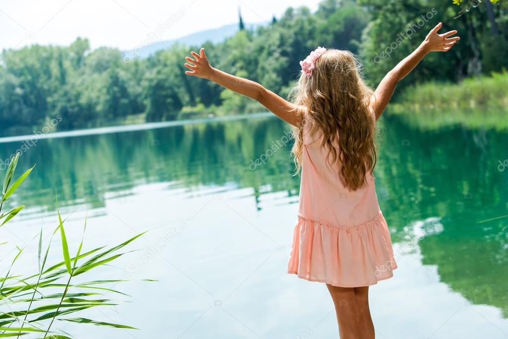 Girl standing at lakeside with open arms.