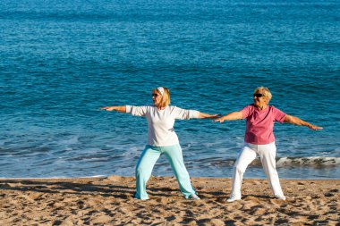 Senior ladies doing yoga on beach. clipart