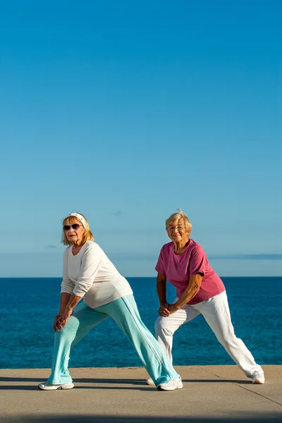 Starszych kobiet robi rozciągające ćwiczenia na wybrzeżu. — Zdjęcie stockowe