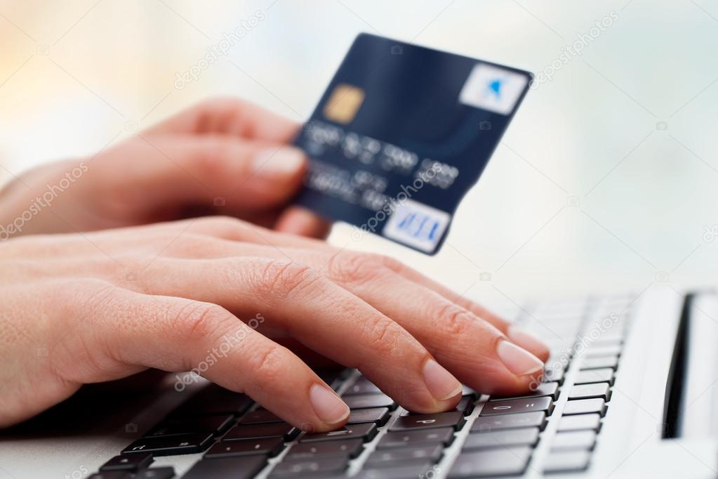 Hand typing on laptop with credit card.