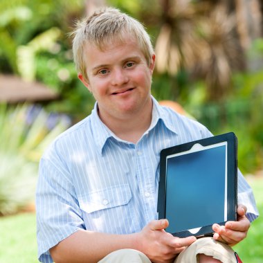 Handicapped boy holding tablet outdoors. clipart