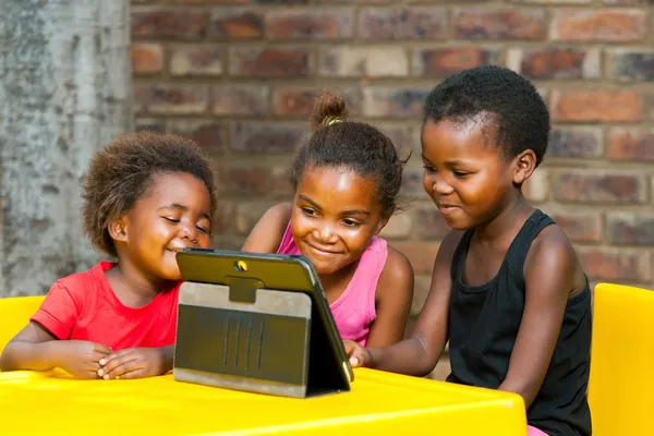 Tři africké děti spolu hráli na tabletu. — Stock fotografie