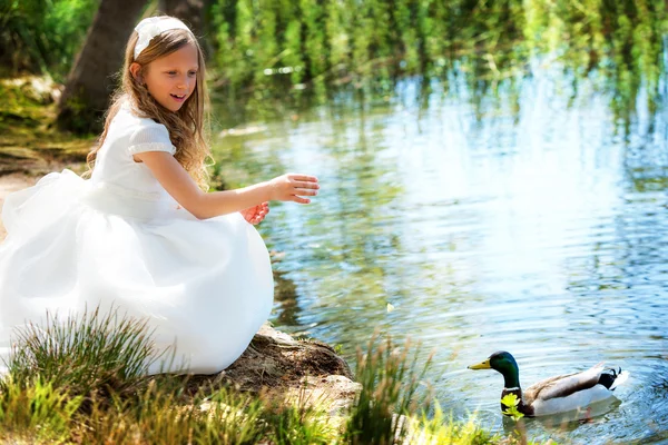 Süßes Mädchen im weißen Kleid füttert eine Ente. — Stockfoto