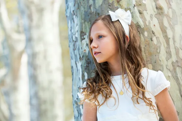 Chica en blanco de pie junto al árbol . — Foto de Stock