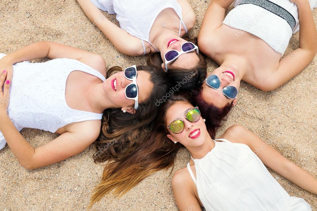 Cute teen girls joining heads together on sand.