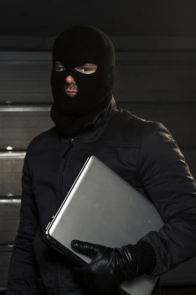 Хакер в маске держит компьютер — стоковое фото