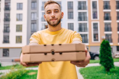 Kamerayı teslim ederken elinde karton kutularla caddede duran yakışıklı bir teslimatçının portresini çekmek. Erkek kurye müşteriye pizza veriyor..