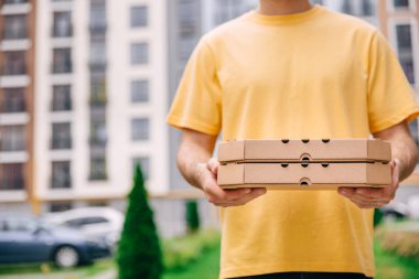 Pizza teslimatçısı şehrin arka planında pizza kutuları tutuyor.